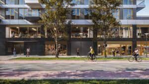 Moderne gevel van het gebouw aan de H.J.E. Wenckebachweg met winkels, een sportschool en mensen op straat en fietsen.